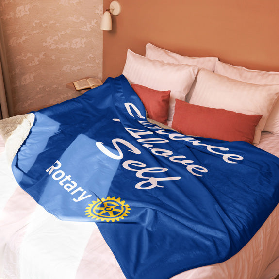 Rotary sherpa blanket styled on a bed with decorative pillows, showing both logo placement and edge detailing.