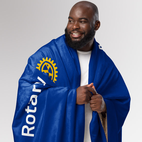 Smiling man wrapped in the Rotary “Service Above Self” sherpa blanket with visible text and logo.