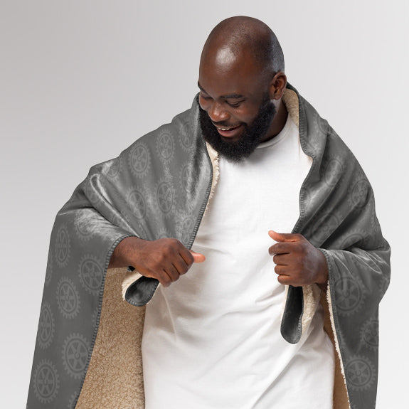 Man unfolding the Rotary sherpa blanket to show its soft sherpa lining and outer Rotary-themed design.