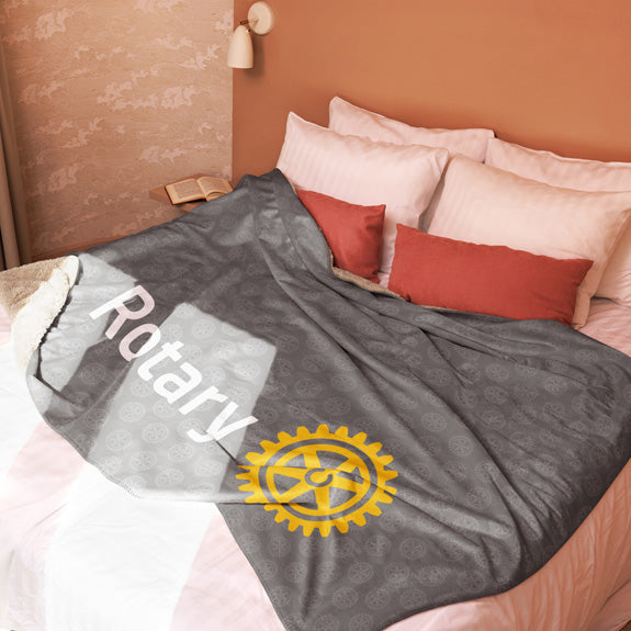 Rotary sherpa blanket styled on a bed with decorative pillows, showing both logo placement and edge detailing.