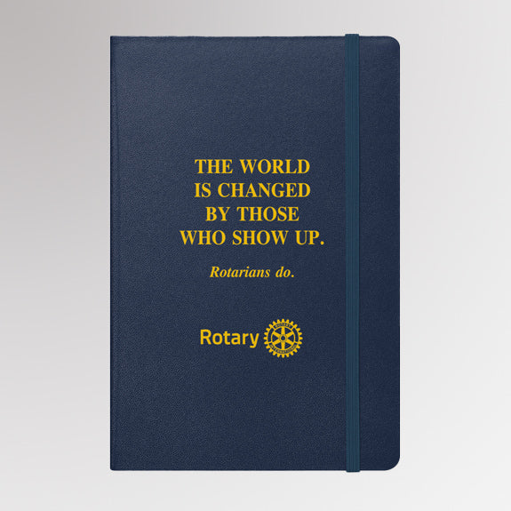 Rotary notebook with gold foil quote “The world is changed by those who show up. Rotarians do.” and the Rotary International Masterbrand logo on a navy blue hardcover.
