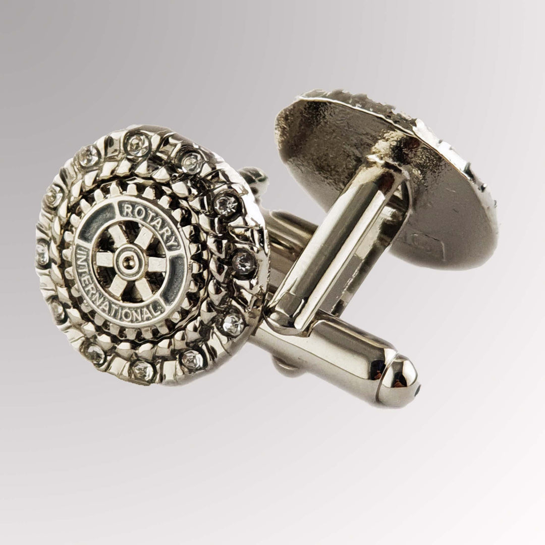 A silver finish cuff link featuring Rotary International's Mark of Excellence logo and white imitation stones.