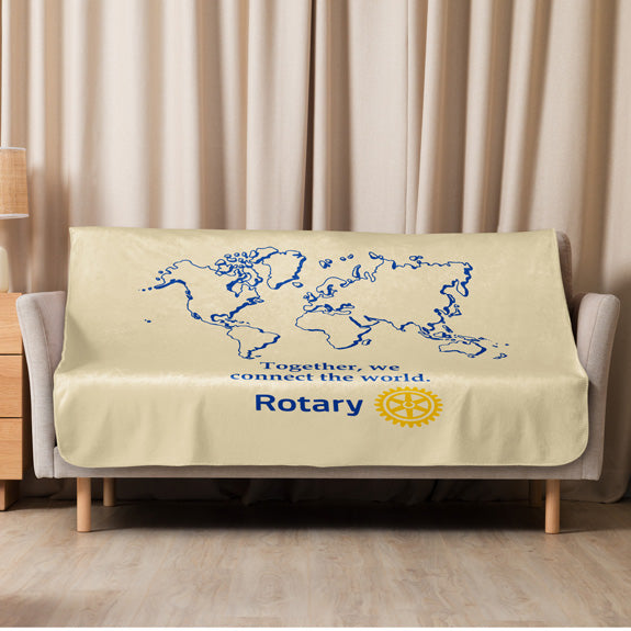 Cream-colored Rotary sherpa blanket featuring a world map design, “Together We Connect the World” message, and the simplified Rotary Masterbrand logo, spread across a sofa.