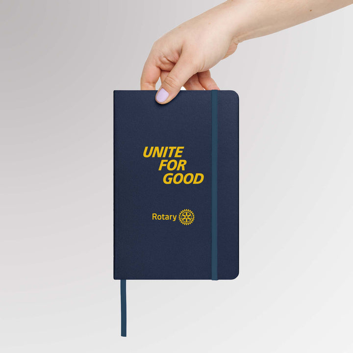 Hand holding the “Unite for Good” Rotary notebook, showing the front cover design, size, and elastic closure.