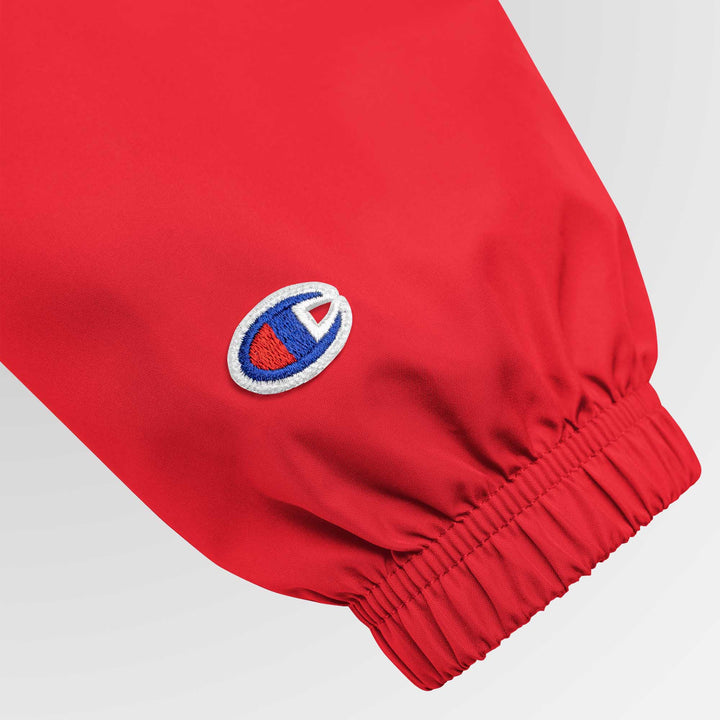 Close-up of the left sleeve of the red Champion jacket, highlighting the embroidered Champion “C” logo above the elastic cuff.