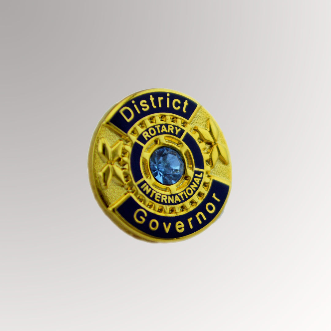 A gold-plated District Governor Pin featuring a blue stone and the traditional Rotary logo.