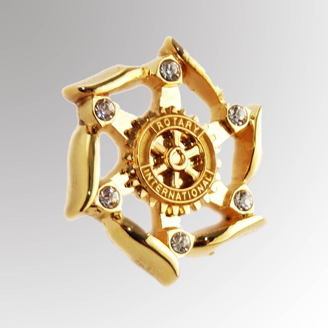 A gold-plated Fancy Stone Pin featuring Rotary International's Mark of Excellence logo with white imitation stones.