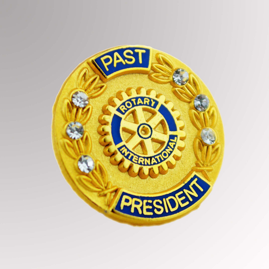 A gold-plated Past President pin featuring a matte background, six white imitation stones, and the traditional Rotary logo.