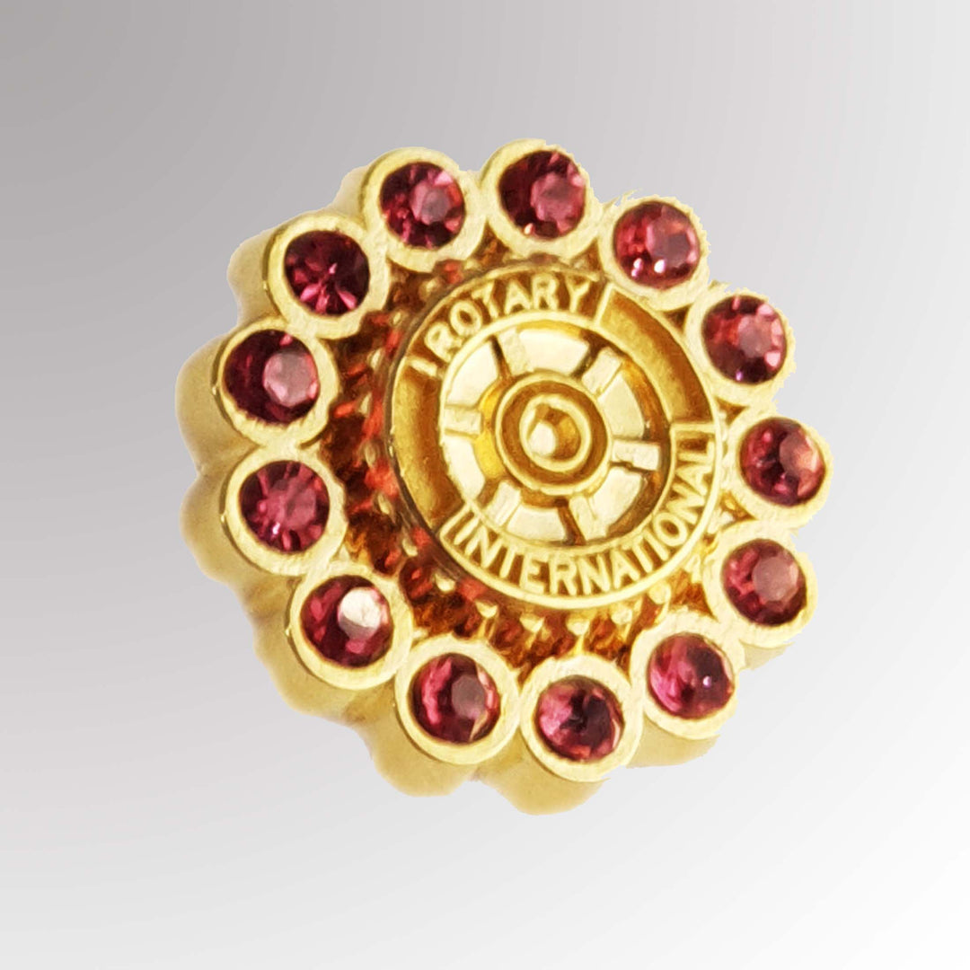 A gold-plated Fancy Rotary Pin featuring Rotary International's Mark of Excellence logo with pink imitation stones.